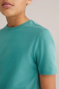 Tirkīza krāsas kokvilnas T-krekls ar īsām piedurknēm, apaļu kakla izgriezumu un gludu tekstūru. Minimāli šuvju detalizējumi ap plecu un piedurkņu malām.