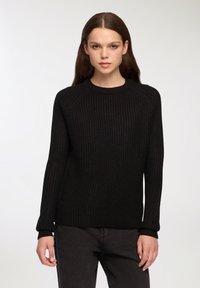 Maglione nero lavorato a maglia con scollo rotondo, texture a coste, maniche lunghe e vestibilità rilassata, abbinato a jeans scuri.