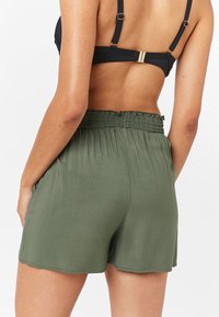 Shorts vert kaki avec une taille smockée, fabriqués dans un tissu léger. Avec des poches latérales et un ourlet décontracté.