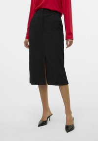 Černá midi sukně z měkké tkaniny s předním rozparkem, doplněná vysokým pasem a dvěma bočními kapsami. Spárována s černými špičatými podpatky.