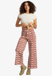 Red and white patterned wide-leg pants with a floral design, made of cotton, featuring a high waist and a raw hem finish. Paired with tan footwear.