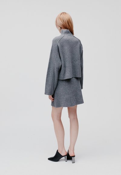 Grauer, gerippter Strickpullover mit hohem Kragen, kombiniert mit einem passenden Rock. Schwarze Mules mit transparentem Blockabsatz runden den Look ab.