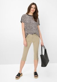 Haut à imprimé léopard avec des manches courtes, accents noirs, pantalons capri beiges, sandales ouvertes noires et un sac fourre-tout noir.