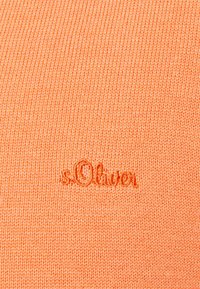 Tissu tricoté orange avec un petit logo brodé "s.Oliver" en fil légèrement plus foncé centré sur la surface.