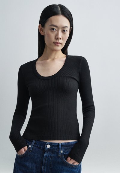 Sort ribbet langærmet top med rund udskæring, kombineret med blå denimjeans. Stoffet har et struktureret mønster.