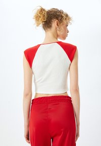 Camiseta sin mangas cortada con cuerpo blanco y paneles de hombros rojos; textura suave y ribeteada; combinada con pantalones rojos de tiro alto.