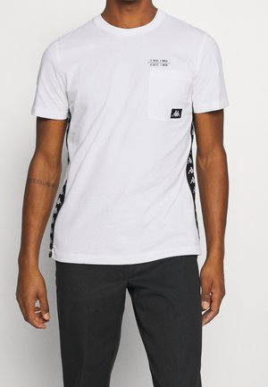 Biała koszulka z krótkim rękawem i kieszonką, z czarnymi akcentami po bokach i brandingiem. Bawełnowy materiał w luźnym kroju i okrągłym dekolcie.