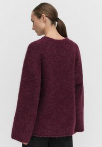Burgundy fluffig tröja med lös passform, rund halsringning och vida ärmar. Tillverkad av ett mjukt, texturerat tyg.