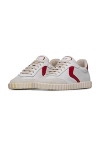 White sneakers with red accents, perforated upper, suede details, beige laces, and a textured rubber sole with a wavy pattern.