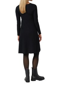 Robe noire à manches longues côtelées avec une jupe évasée, assortie à des bottines noires avec un matériau texturé et des panneaux élastiques sur les côtés.