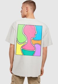 Hvid oversized t-shirt med et farverigt abstrakt grafik på ryggen, bestående af former i pink, grøn, orange og lilla omridset i sort.