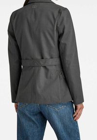 Harso bleiseri, joka on valmistettu teksturoidusta kankaasta, ja siinä on istuva siluetti, vyöllinen vyötärö ja hienovarainen pystyraitakuosi.