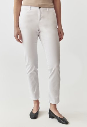White slim-fit trousers made of smooth fabric, featuring a button closure and standard pockets, paired with black low-heeled shoes.