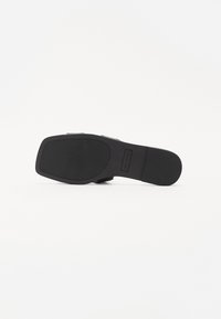 Chaussures noires à semelle plate, présentant un motif texturé pour l'adhérence, un talon renforcé et un design supérieur lisse.