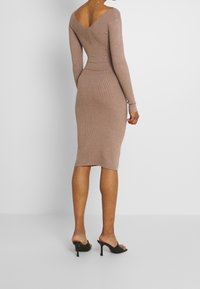 Abito midi a coste in taupe chiaro con scollatura a V sul retro, maniche lunghe e silhouette aderente. Indossato con sandali neri con tacco alto.