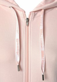Helle rosa Kapuzenjacke mit weicher Textur. Verfügt über einen silbernen Reißverschluss und Kordeln mit "Bench"-Branding in Weiß auf einem Ripsband-Akzent.