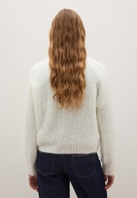 Lightweight, fluffy white sweater with a ribbed texture, round neck, and long sleeves, paired with dark blue denim jeans.