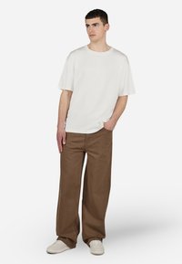 White short-sleeve t-shirt with a crew neckline paired with brown wide-leg pants and white sneakers. Smooth fabric with minimal design.