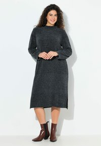 Robe tricotée grise avec un col montant, des manches longues et des fentes sur les côtés ; associée à des bottines chevilles marron foncé avec des panneaux élastiques sur les côtés.