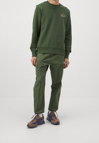 Grön sweatshirt med rund halsringning och ribbade ärmslut, kombinerad med matchande cargobyxor med sidofickor och elastiska benfållar.