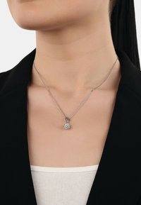 Collana d'argento con un pendente circolare e scintillante su una catena sottile. Il pendente presenta una superficie testurizzata, simile a un cristallo.