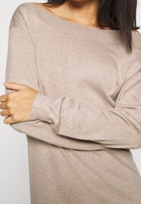 Maglione off-shoulder beige chiaro, realizzato in un morbido tessuto a maglia testurizzato. Presenta maniche lunghe e polsini a costine.