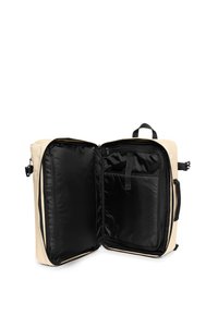 Mochila rectangular beige con dos compartimentos con cremalleras negras, forro interior negro, un bolsillo delantero y asa superior para llevar.