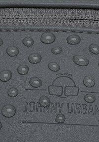 Gouttes d'eau sur surface grise texturée près de la fermeture éclair, embossée avec le logo "Johnny Urban" et un graphisme de sac.