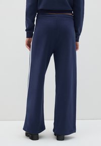 Marineblauwe wijde broek van een zacht materiaal met een geribbeld elastische tailleband en witte zijstrepen. Rechte zoom en lichte elasticiteit voor extra comfort.