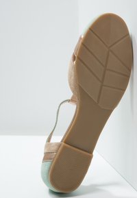 Sandales beige en daim avec une bride supérieure vert menthe, dotées d'une semelle en caoutchouc texturée, d'un bout arrondi et d'une bride de cheville réglable.