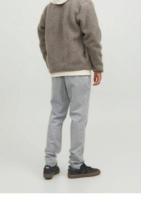 Giacca in polar grigia e morbida con un cappuccio bianco sotto, abbinata a pantaloni a righe grigie chiare e sneakers nere. Texture morbida, vestibilità rilassata.