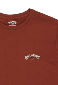 T-shirt w kolorze rdzy z bawełny, z okrągłym dekoltem i małym białym logo "Billabong" na lewej stronie klatki piersiowej. Gładka faktura, krótkie rękawy.