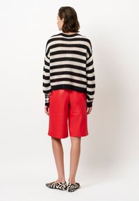 Zwart en crèmekleurige gestreepte trui, rode leren shorts en ballerina's met dierenprint. Losse pasvorm, gebreide textuur en shorts tot halverwege de dij.