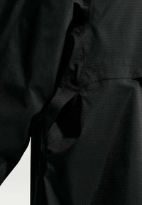 Κοντινό πλάνο μαύρου υφάσματος που δείχνει ραφές και ραφές με διακριτή υφή και ελαφριά γυαλάδα υπό απαλό φωτισμό.