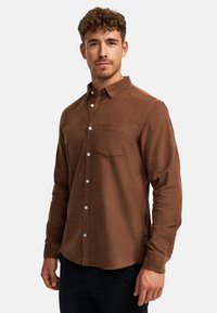 Barna kordbársony hosszú ujjú ing fehér gombokkal és mellzsebbel. Puha textúrájú, laza szabású.