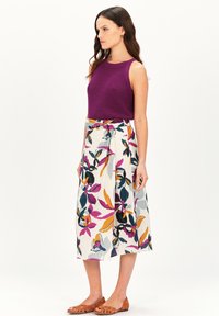 Un top de tirantes de punto acanalado morado combinado con una falda crema que presenta coloridos estampados florales. Sandalias planas marrones completan el conjunto.