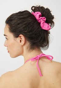Rozā scrunchie ar krunkainu tekstūru, valkāta haotiskā bunā, ar atbilstošu sasietu loku aizmugurē pie kakla. Izpeldējusi gluda āda.
