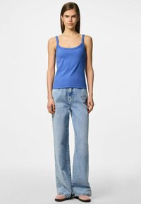 Top sin mangas azul con escote cuadrado, hecho de una tela texturizada, combinado con jeans de campana de lavado claro y zapatos rosa suave.