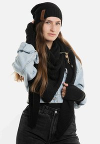 Zwarte gebreide beanie, oversized zwarte sjaal en vingerloze handschoenen. Draagt gecombineerd met een licht denim jack en high-waisted zwarte jeans.