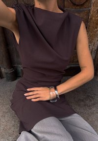 Robe drapée marron foncé avec un col rond et des épaules froncées, assortie à un pantalon large gris et un bracelet aleatoire en argent et transparent.
