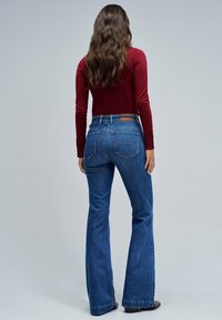 Jeans in denim blu a gamba svasata con vita media e tasche posteriori, abbinati a una maglietta a maniche lunghe bordeaux.