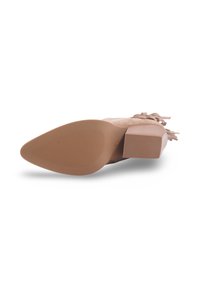 Chaussure à talon bloc avec un dessus en nubuck beige clair, semelle texturée et pompons décoratifs sur le côté. Présente un design à bout pointu.