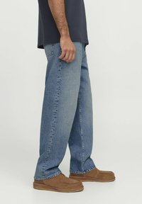 Helle blaue Jeans aus Denim mit lockerer Passform, geradem Bein, dezentem Verblassen und im klassischen fünf-Taschen-Stil. Getragen mit braunen Hausschuhen.