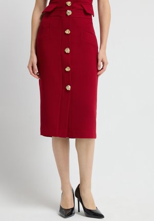 Rode kokerrok met een aansluitend ontwerp, voorzien van gouden knopen aan de voorkant en twee zijzakken; gladde textuur en kniehoogte.