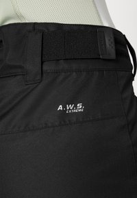 Pantaloni negri de exterior, cu un talie texturată și un eticheta de marcă care spune "A.W.S. EXTREME." Materialul este neted, cu un design ajustat.