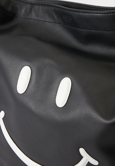 Surface en cuir noir avec des formes ovales blanches cousues ressemblant à des yeux et une ligne courbée formant un visage souriant.