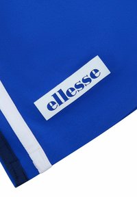 Niebieski odzież o gładkiej fakturze, z białym akcentem i prostokątną metką z logo "ellesse" w ciemnoniebieskim kolorze.