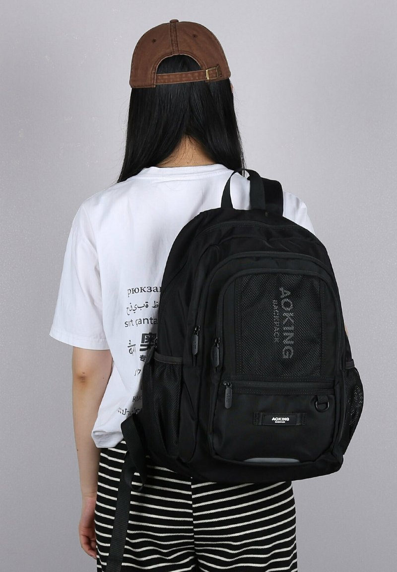 Zaino nero realizzato in tessuto resistente, con molteplici scomparti, tasche laterali in rete e spallacci regolabili. Presenta un logo sulla parte anteriore.