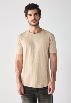 Beige short-sleeve t-shirt with a round neckline, made of lightweight fabric. Features a subtle texture, paired with dark jeans.