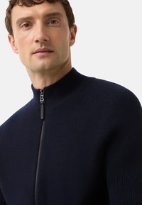 Námořnický svetr na zip s vysokým límcem, žebrovanou texturou na ramenou a hladkou látkou na těle s elegantním kovovým zipem.